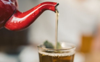 Tea from red kettle being poured into clear glass